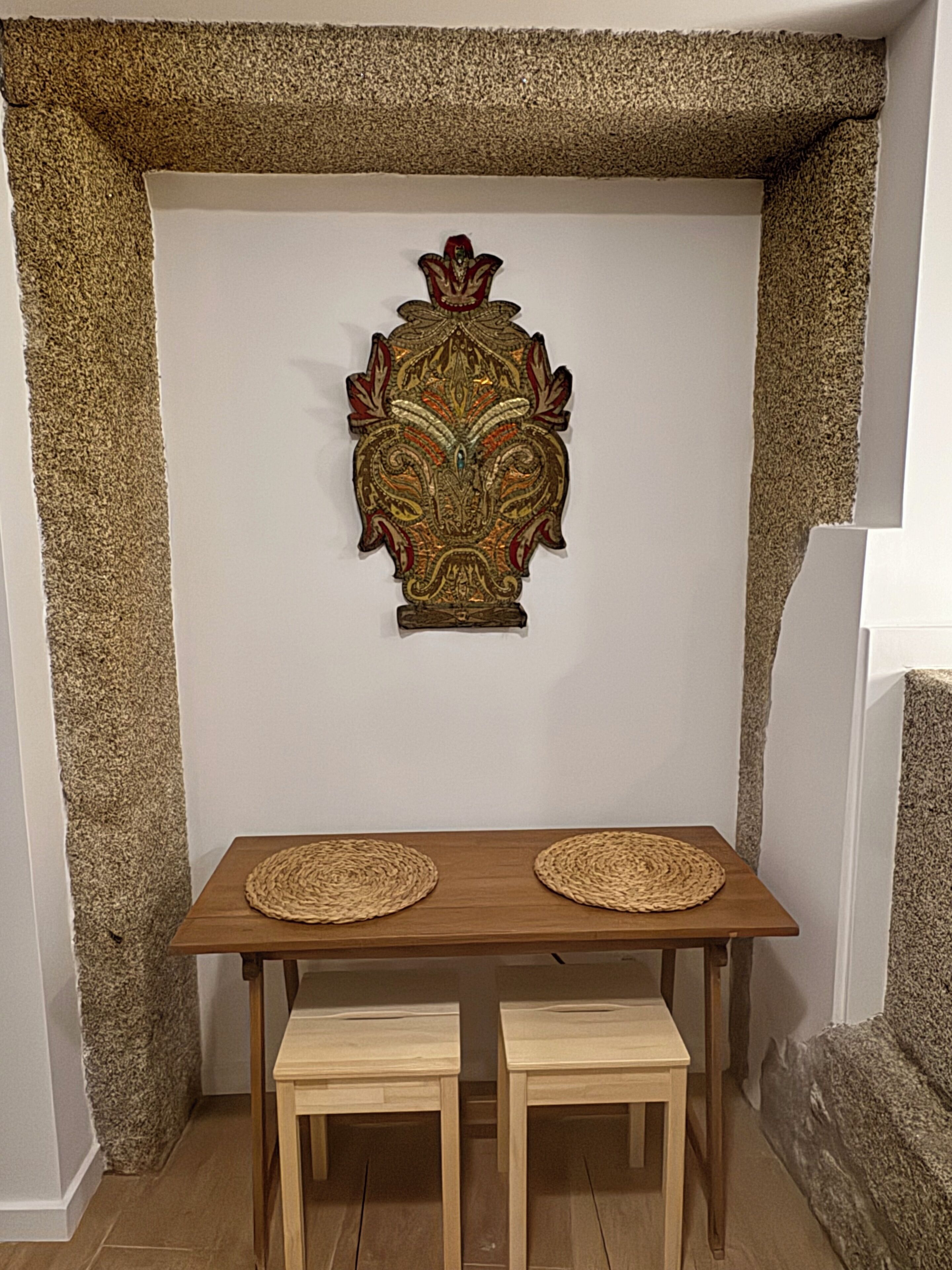 Una habitación con una pared blanca, un emblema decorativo y una mesa de madera con dos taburetes.