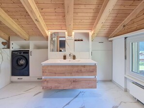 Eine moderne Küche mit eingebauter Waschmaschine, Holzbalkendecke und einem großen Fenster.