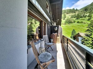 Ein Balkon mit Holzkubeln und Tisch, der auf eine grüne Landschaft mit Bäumen und einem Berg blickt.