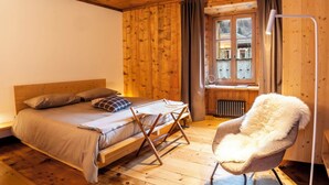 A wooden cabin room with a bed, a chair, and a window with curtains. - Beautiful apartment for 5 people with WIFI and TV (Bormio)