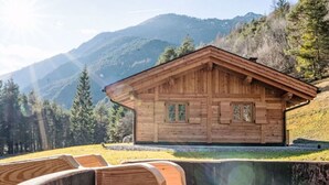 Eine Holzhütte mit geneigtem Dach vor einer Bergkulisse.