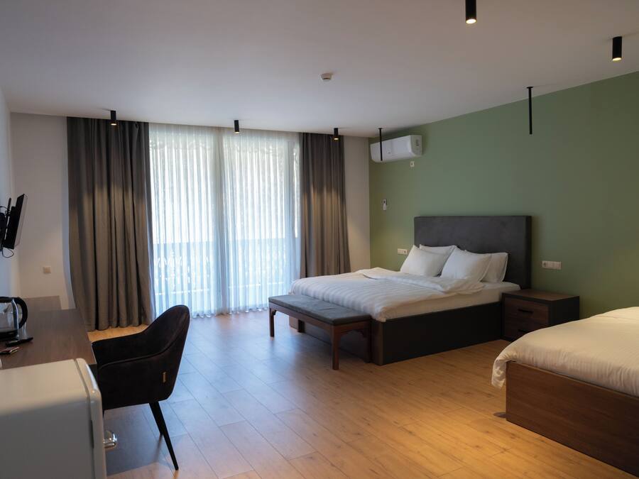 Una habitación de hotel con cama, escritorio, silla y ventana con cortinas.