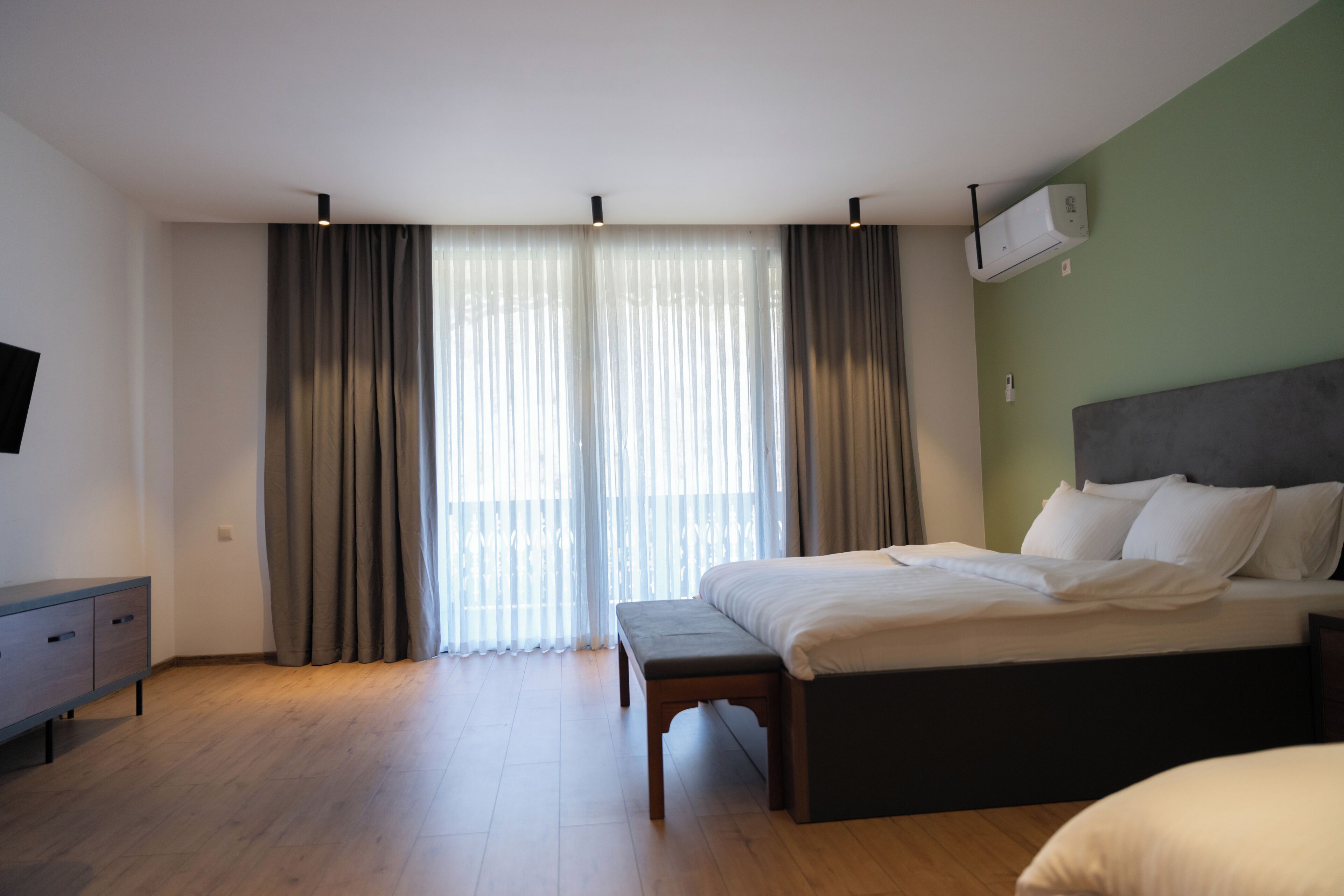 A bedroom with a bed, a bench, a TV, and a window with curtains.