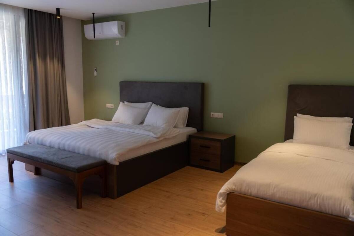 A bedroom with two beds, a bench, and a bedside table.