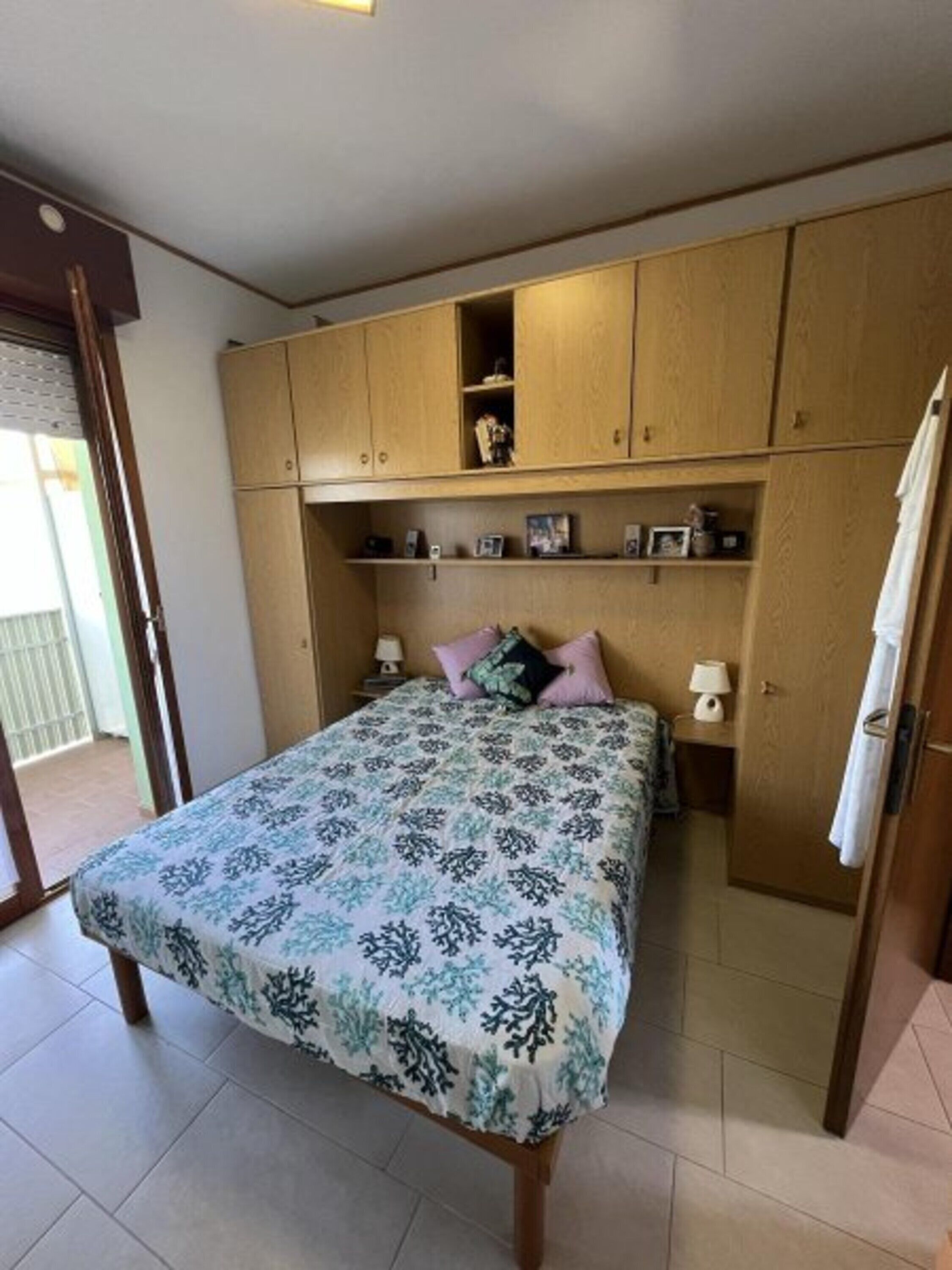 A bedroom with a bed, wooden wardrobe, and a small table with a lamp.