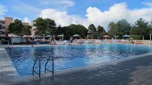 Une piscine entourée d’arbres et de bâtiments, avec des chaises longues et des parasols.