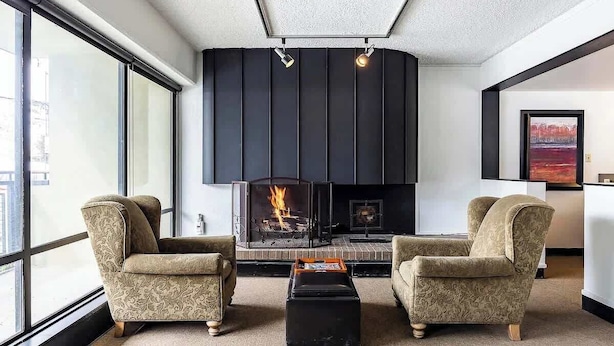 Una sala de estar moderna con chimenea, dos sillones, una mesita de centro y ventanas amplias.