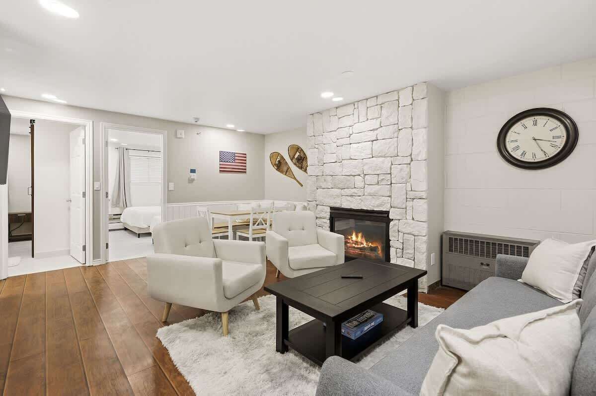 Una sala de estar con chimenea, paredes blancas y un reloj.