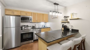Una cocina moderna con electrodomésticos de acero inoxidable, armarios de madera, una isla central con taburetes altos y una lámpara colgante.