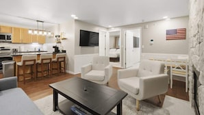 Una sala de estar moderna con comedor, cocina y televisor montado en la pared.