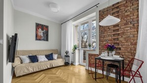 En moderne stue med sofa, spisebord og stole. Der er en murstensvæg og et vindue med gardiner.