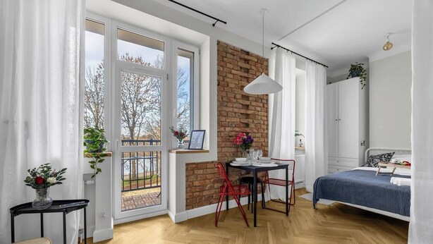Et moderne soveværelse med en murstensvæg, et spiseområde med bord og stole, samt et stort vindue med udsigt til træer.