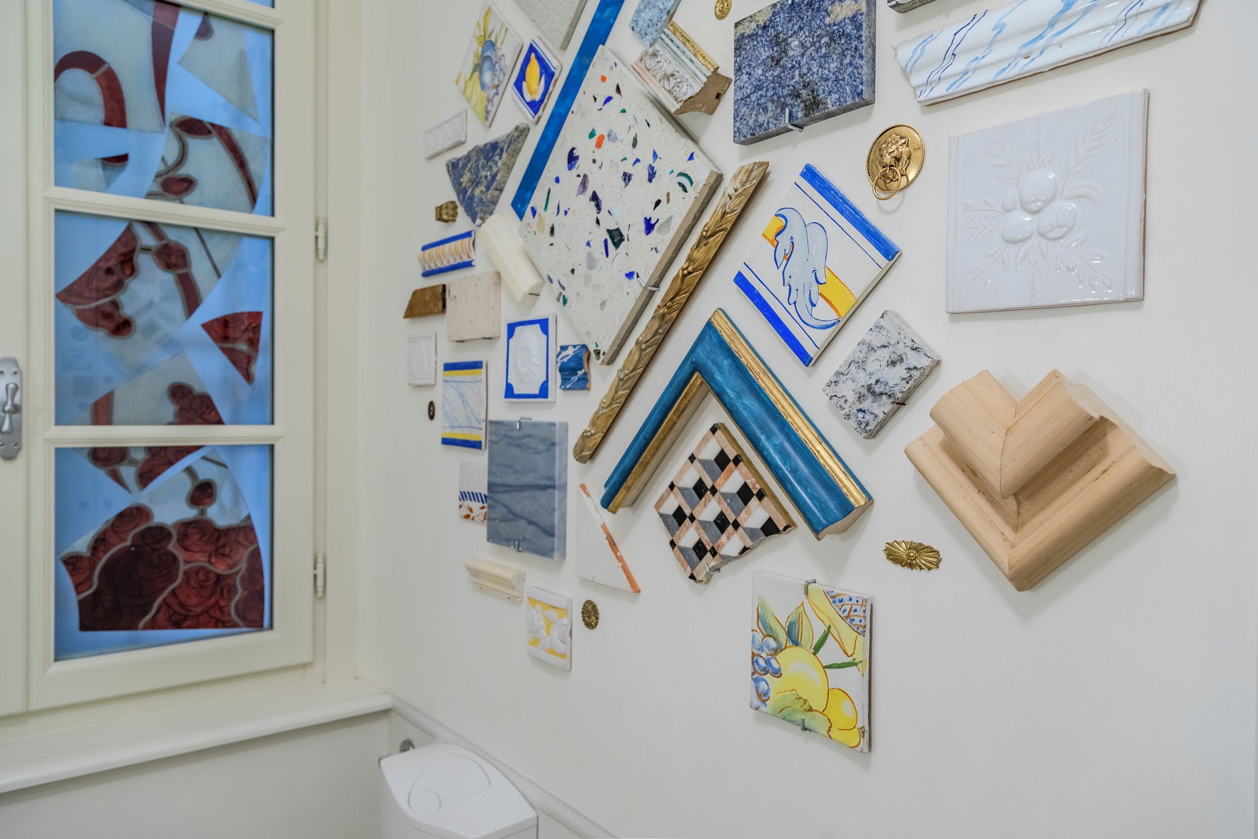 Una pared decorada con varias obras de arte y elementos decorativos, como cuadros enmarcados, azulejos y una pequeña escultura de madera.