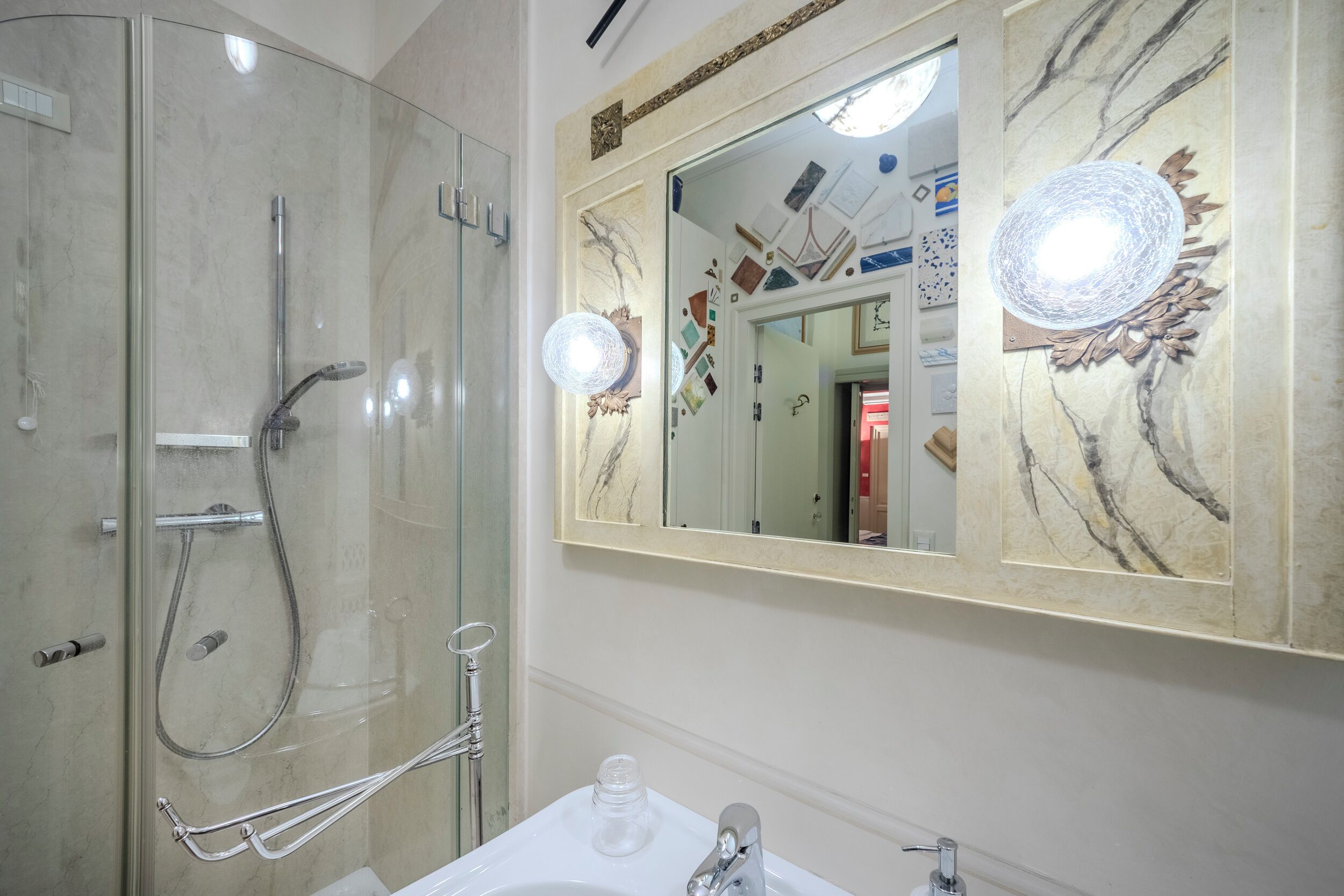 A bathroom with a glass-enclosed shower, a sink with a mirror above it, and a decorative wall piece.