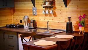 Un interior de madera con una zona de cocina que incluye una estufa, una cafetera y una repisa con tazas.
