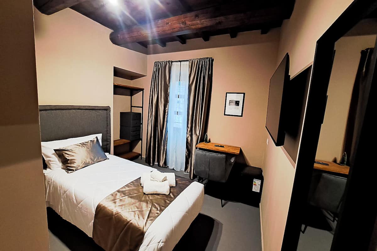 Habitación de hotel con cama, escritorio, silla, televisor y espejo.