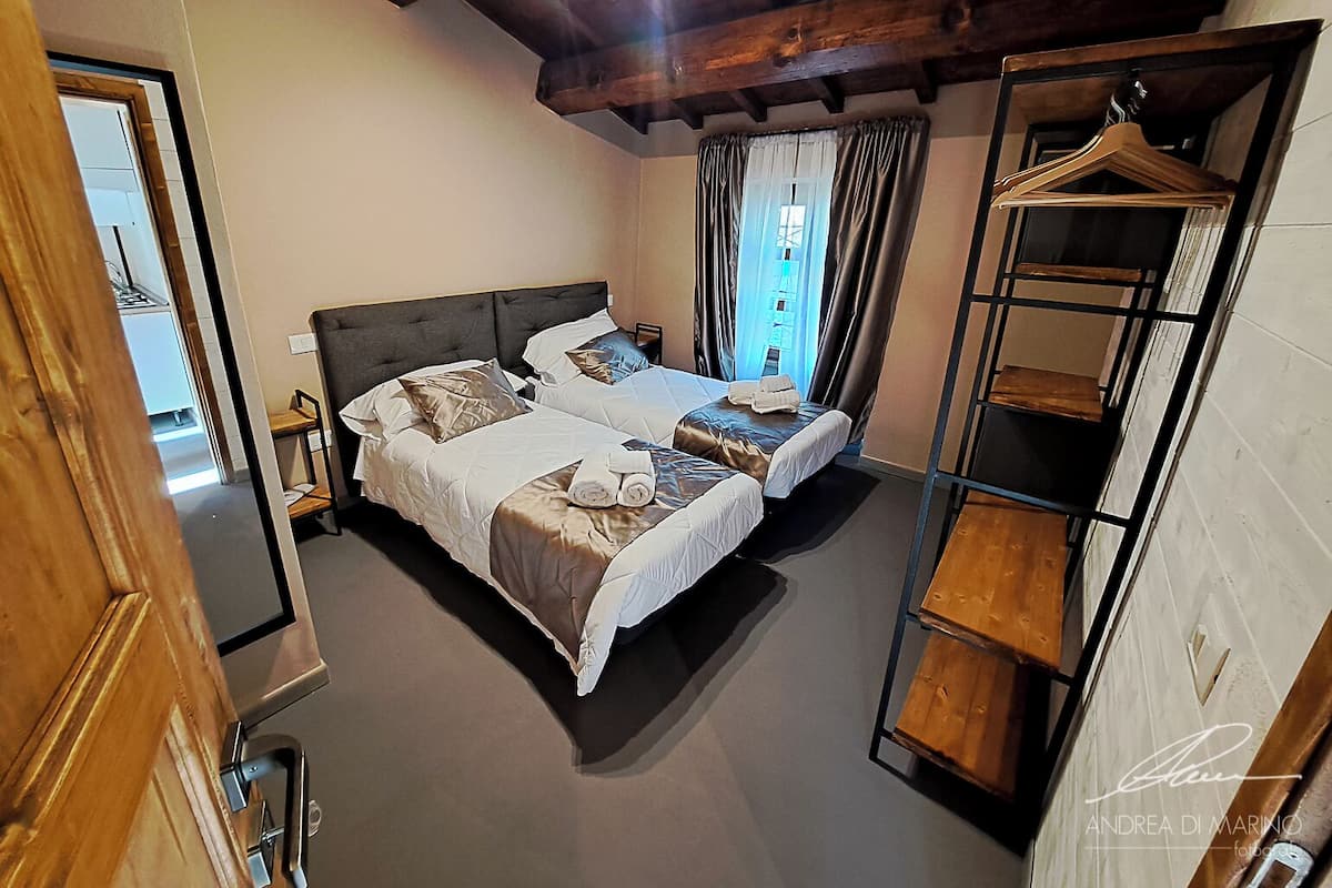 Un dormitorio con dos camas, techo de madera, ventana con cortinas y un armario de madera.