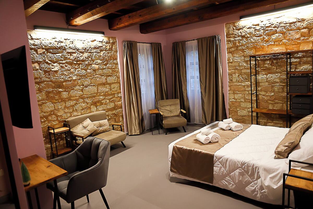 Habitación de hotel con pared de piedra, una cama con toallas, un sofá, una silla y una mesita.