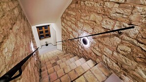 Un escalier étroit aux murs de pierre, avec une petite fenêtre en haut.
