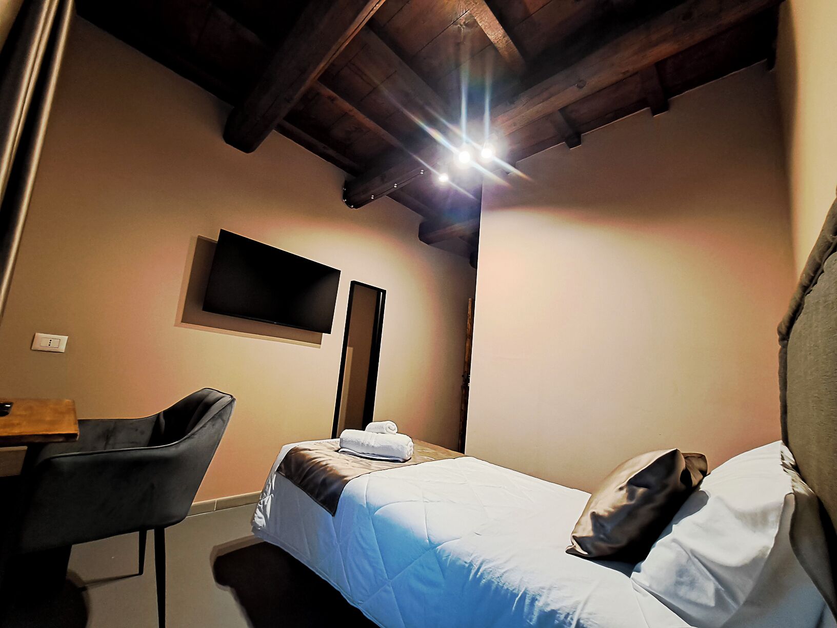 Una habitación pequeña y acogedora con una cama, un escritorio y una silla. Hay un televisor de pantalla plana montado en la pared.