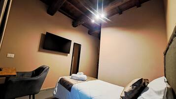 Una habitación pequeña y acogedora con una cama, un escritorio y una silla. Hay un televisor de pantalla plana montado en la pared.