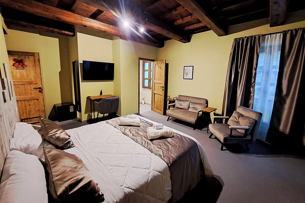Habitación de hotel con una cama grande, un escritorio con silla, un sofá y un televisor montado en la pared.