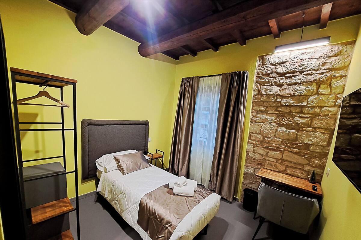 Un dormitorio con una cama, un armario de madera, un escritorio y una pared de piedra.