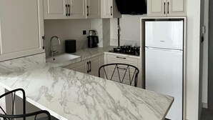 A modern kitchen with white cabinets, a marble countertop, a gas stove, and a built-in oven.