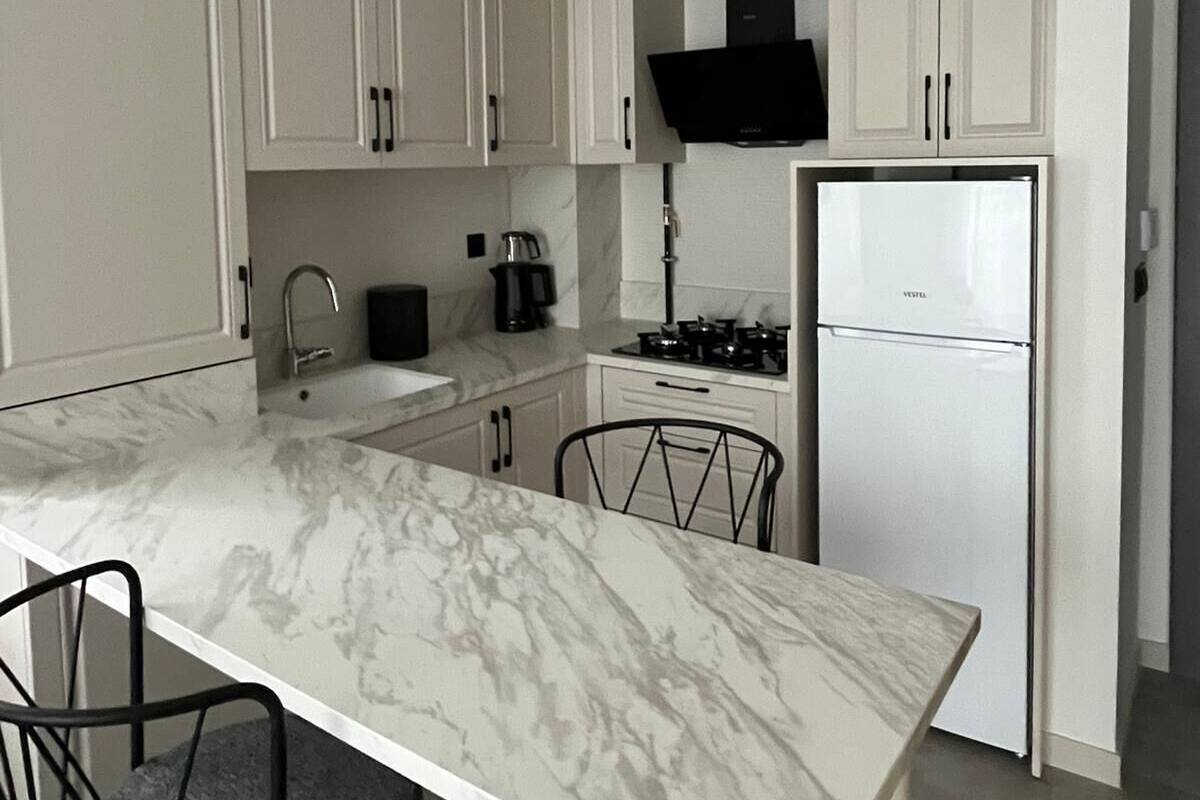 A modern kitchen with white cabinets, a marble countertop, a gas stove, and a built-in oven.