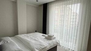 A modern bedroom with a bed, a bedside table, and a window with sheer curtains.