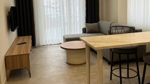 A modern living room with a sofa, a dining table, and a TV on a wooden cabinet.