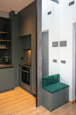 A modern kitchen with dark cabinets, a built-in oven, and a green cushioned bench. - Cozy and Elegant Loft Style 1 Bedroom Apartment in Tbilisi (T'bilisi)