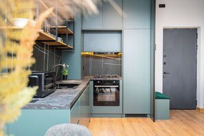 A modern kitchen with built-in appliances, wooden flooring, and a grey door. - Cozy and Elegant Loft Style 1 Bedroom Apartment in Tbilisi (T'bilisi)