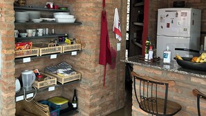 A kitchen with brick walls, shelves with kitchenware, a refrigerator, and a bar area. - Beautiful house in Barão Geraldo (5 min from Unicamp) (Campinas)