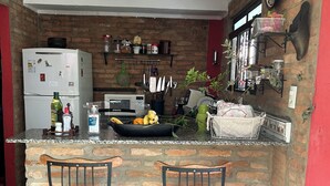 A kitchen with a brick wall, a refrigerator, a sink, and two bar stools. - Beautiful house in Barão Geraldo (5 min from Unicamp) (Campinas)
