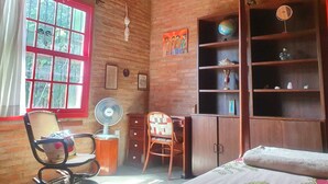 A cozy room with a brick wall, a wooden desk, a bookshelf, a globe, and a bed with a patterned bedspread. - Beautiful house in Barão Geraldo (5 min from Unicamp) (Campinas)
