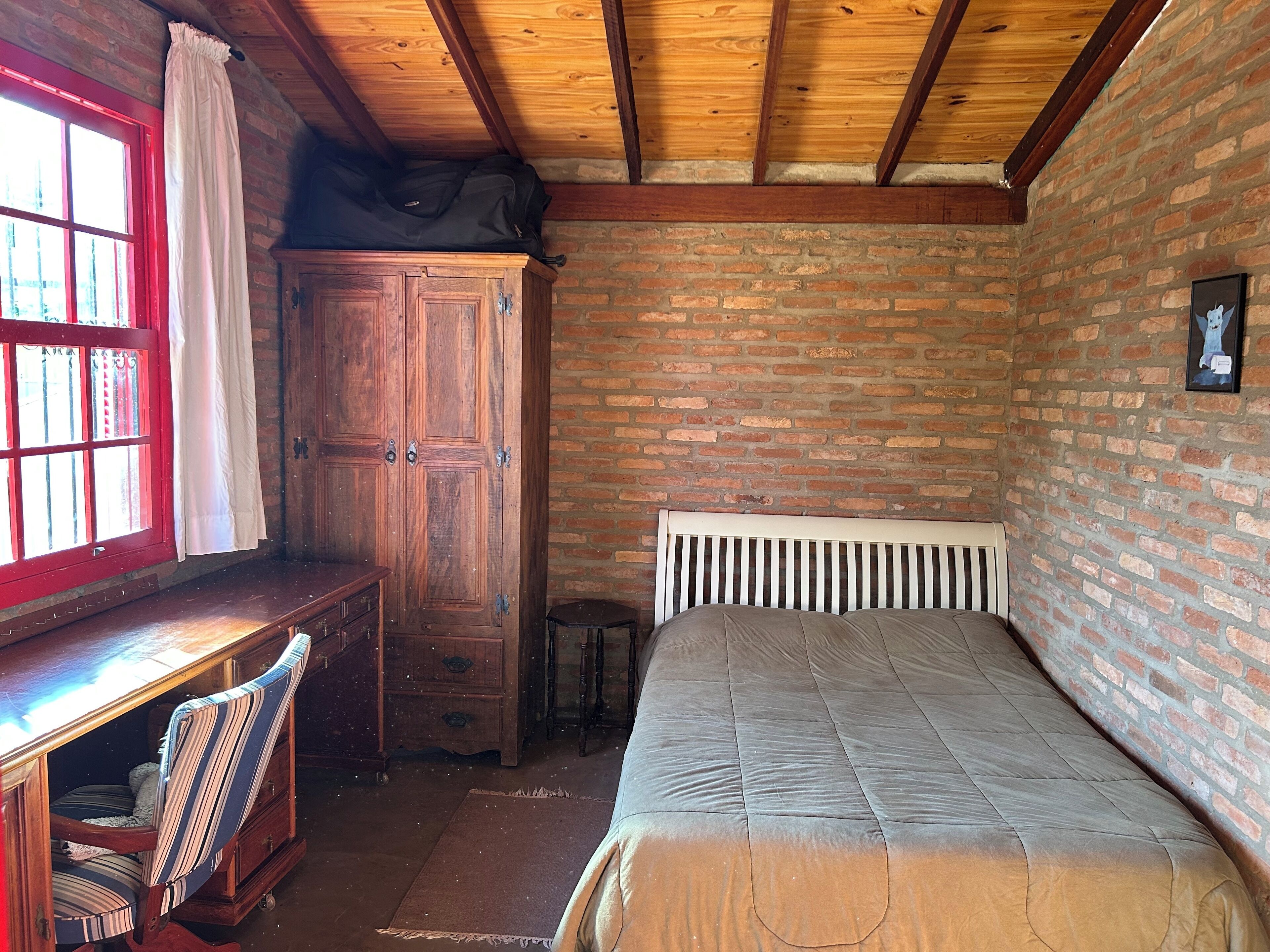 Une pièce avec un bureau en bois, une chaise, un lit avec une tête de lit blanche et un mur en briques.