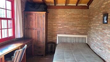Une pièce avec un bureau en bois, une chaise, un lit avec une tête de lit blanche et un mur en briques.