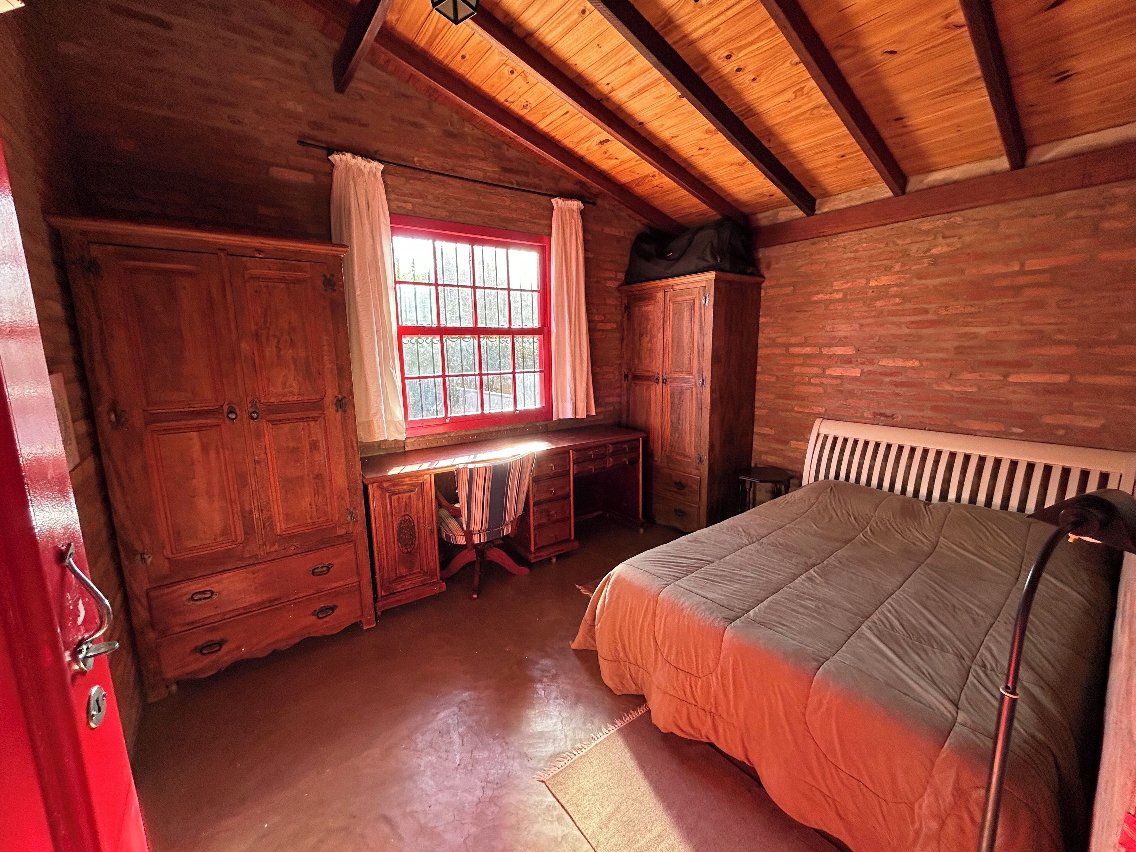 Una habitación rústica de madera con una cama, un escritorio y una ventana con cortinas.