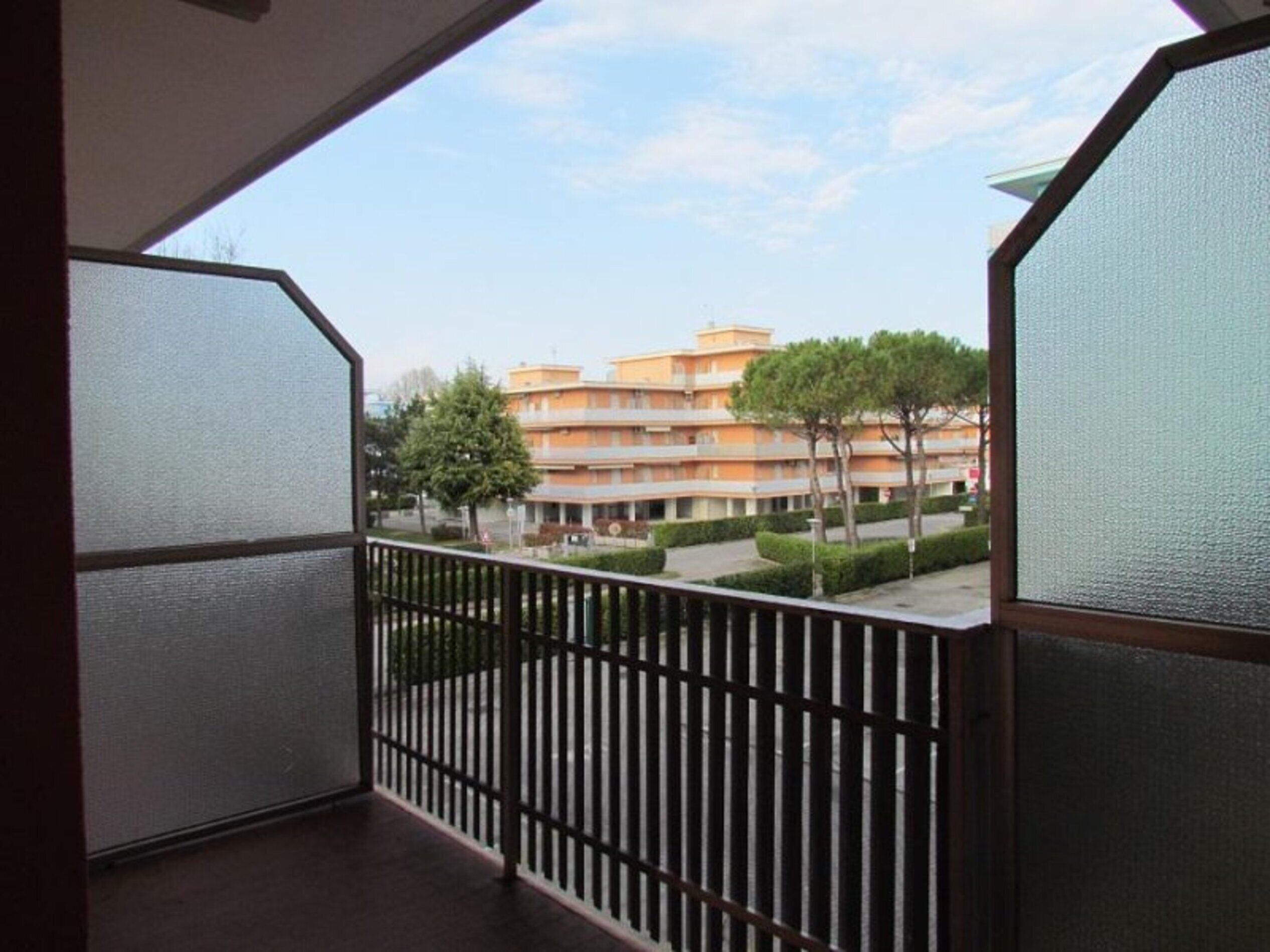 Un balcone con vista su un edificio a più piani dalle facciate arancioni e un cielo sereno.