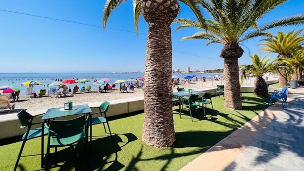 Una veranda fronte spiaggia con tavoli e sedie, palme e ombrelloni.