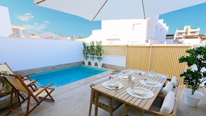 Una terrazza sul tetto con piscina, tavolo da pranzo in legno per quattro persone e poltrone da relax.