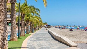 Una passeggiata lungomare fiancheggiata da palme, che conduce a una spiaggia con ombrelloni e persone.