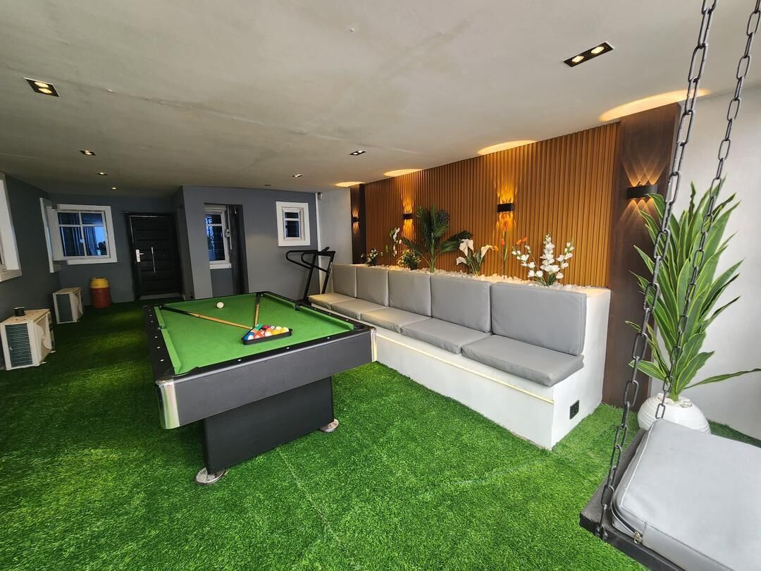 A pool table with a green felt surface, a grey sofa, and a hanging swing chair.