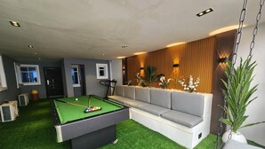 Una mesa de billar con superficie de fieltro verde, un sofá gris y un sillón colgante.