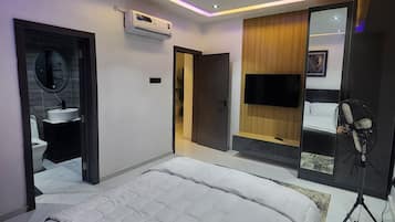 A modern bedroom with a large bed, a built-in TV, an air conditioning unit, and a fan.