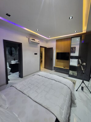 Ein modernes Schlafzimmer mit einem großen Bett, einem eingebauten Fernseher, einer Klimaanlage und einem Ventilator.