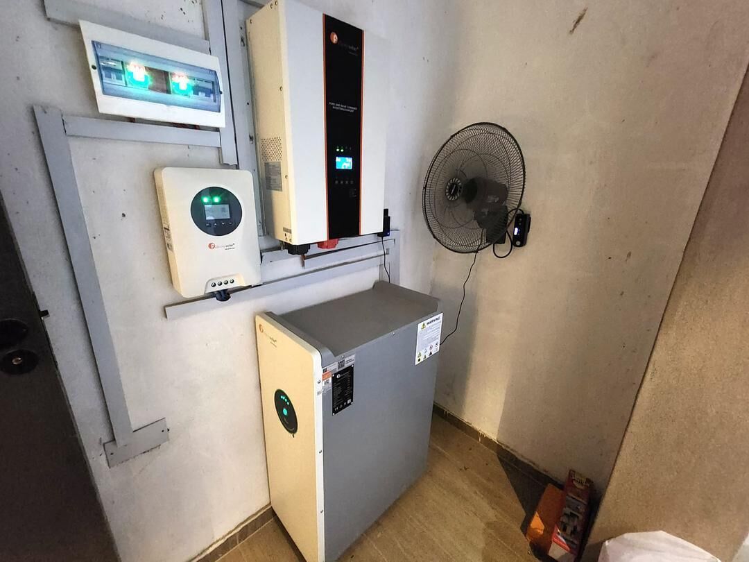 A compact room with a small heater, a wall-mounted fan, and a control panel on the wall.