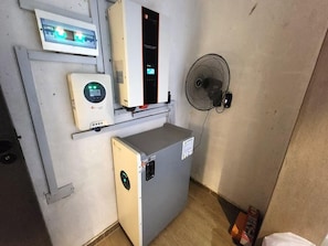 Una habitación compacta con un pequeño calentador, un ventilador de pared y un panel de control en la pared.
