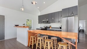 Cozinha moderna com ilha central, banquetas, eletrodomésticos de aço inoxidável e luminárias pendentes.